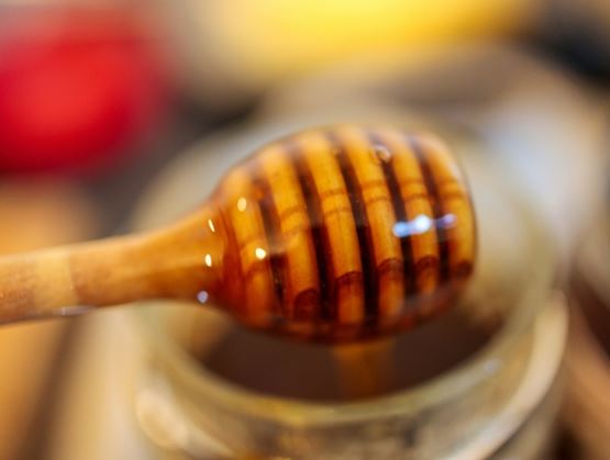 Cuillère en bois nappée de miel doré au-dessus d’un pot.