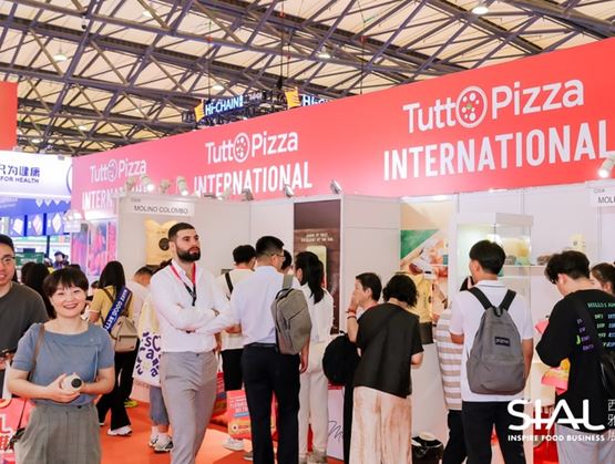A busy TuttoPizza International exhibition booth at a trade show, with many visitors interacting in front of displays and red panels.