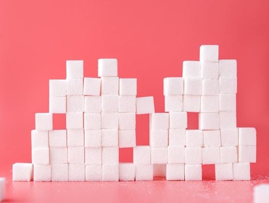 White sugar cubes stacked to form the word “CO2” on a pink background, illustrating the link between sugar and carbon emissions.