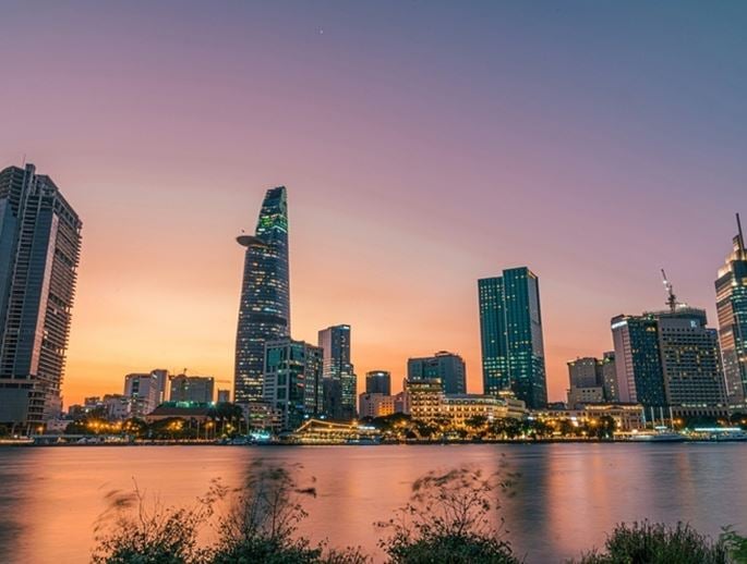 Panoramic view of the Ho Chi Minh City skyline at sunset, with modern skyscrapers reflecting on the river.