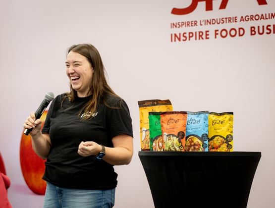 Smiling woman presenting Les Brutes food products with a microphone at a professional event.