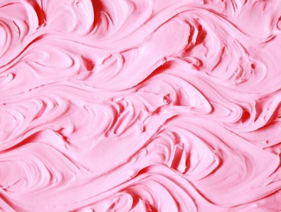Close-up of a pink creamy texture, forming smooth swirls and waves.