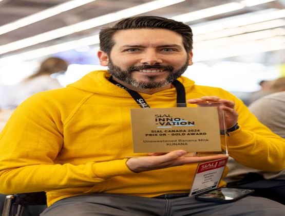 Man in a yellow hoodie holding the SIAL Innovation Canada 2026 Gold Award for Kunana unsweetened banana milk at a trade show.