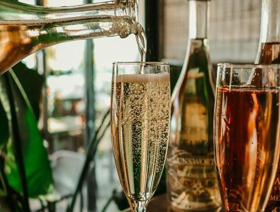 Vin pétillant versé dans une flûte, avec des bouteilles et un verre de rosé en arrière-plan.