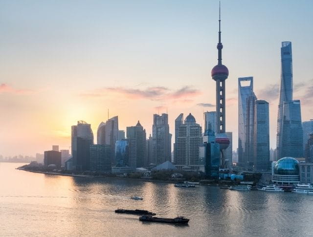 Vue panoramique de la skyline de Shanghai au coucher du soleil, avec la rivière Huangpu en premier plan.