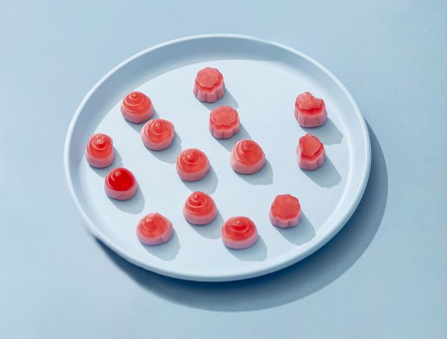 White plate with several small pink candies neatly arranged on a light blue background.