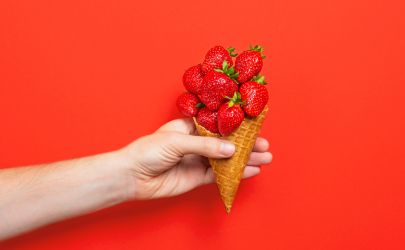 Hand holding an ice cream cone filled with fresh strawberries against a bright red background.