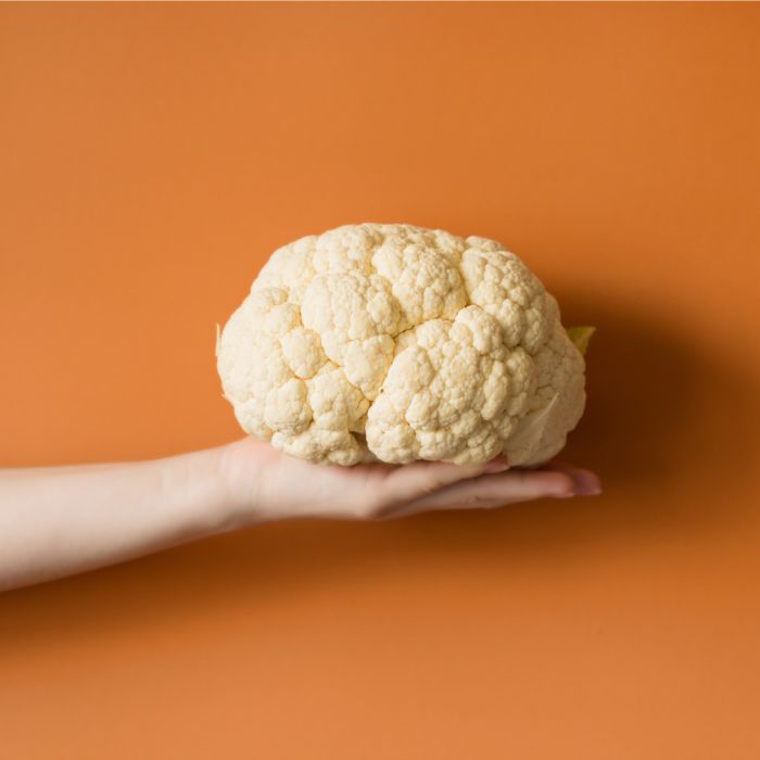 Whole cauliflower held in hand on an orange minimalist background representing plant-based food trend