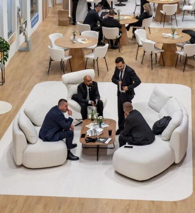 Business meeting between five men in suits in a lounge area at a trade show.