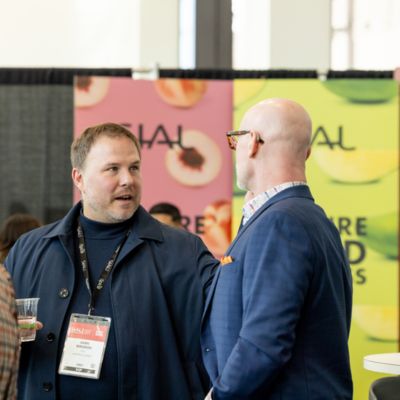 Two professionals talking at an international trade show in front of an Inspire Food Business display.