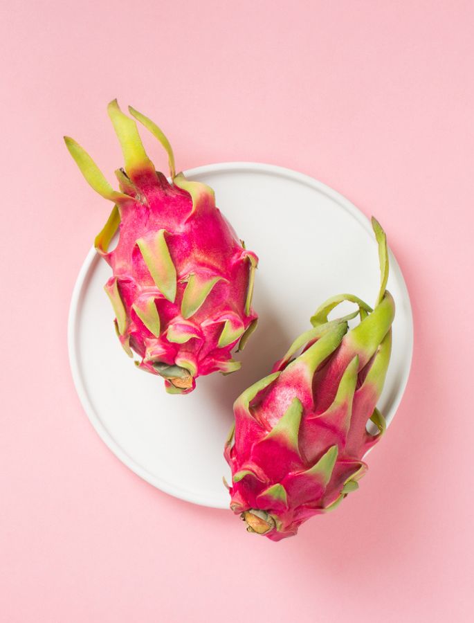 Dragon fruits placed on a white plate on a pink background, minimalist composition.
