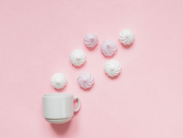 White cup with meringues arranged on a pastel pink background.