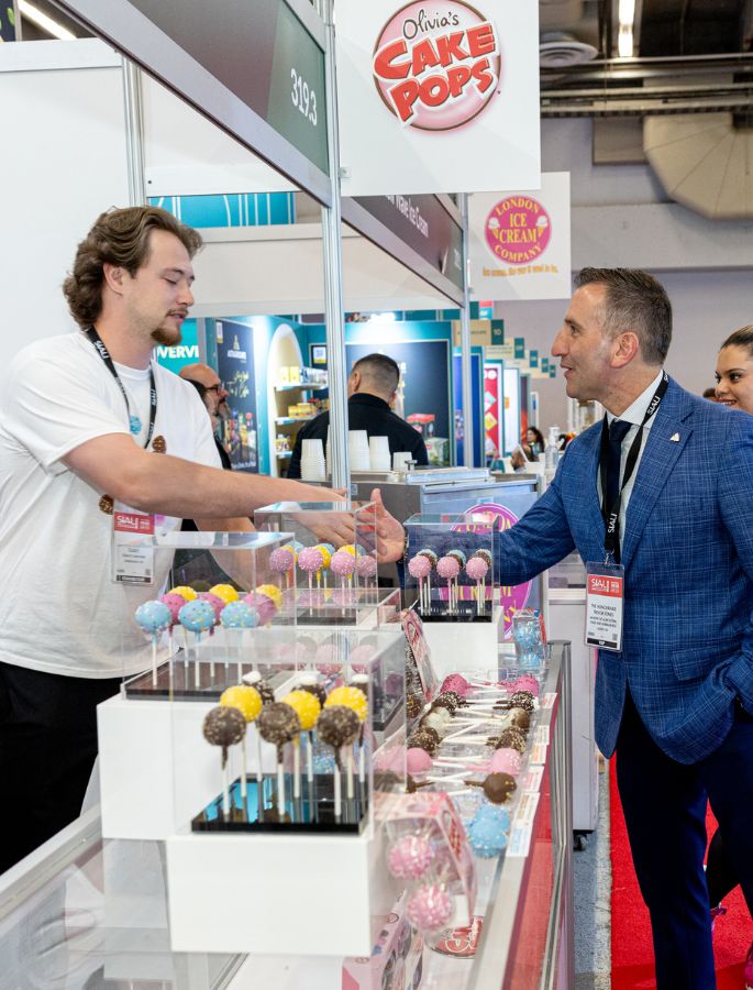 Handshake at the SIAL trade show at Olivia’s Cake Pops booth, with colorful cake pop displays in the foreground.