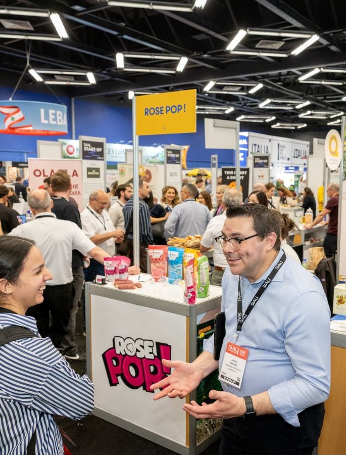 Two attendees talk at the SIAL trade show in front of the ROSE POP! stand, in a busy exhibition hall aisle.