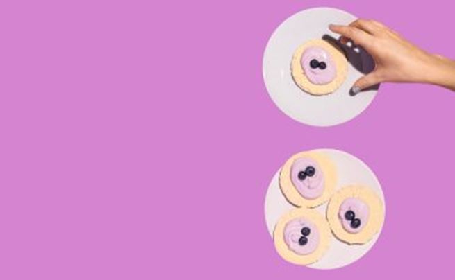 Hand picking a heart-shaped cookie with purple icing and blueberries on a pastel purple background