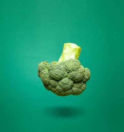 Green broccoli floating in the center on a solid green background, minimalist composition highlighting a fresh healthy vegetable.