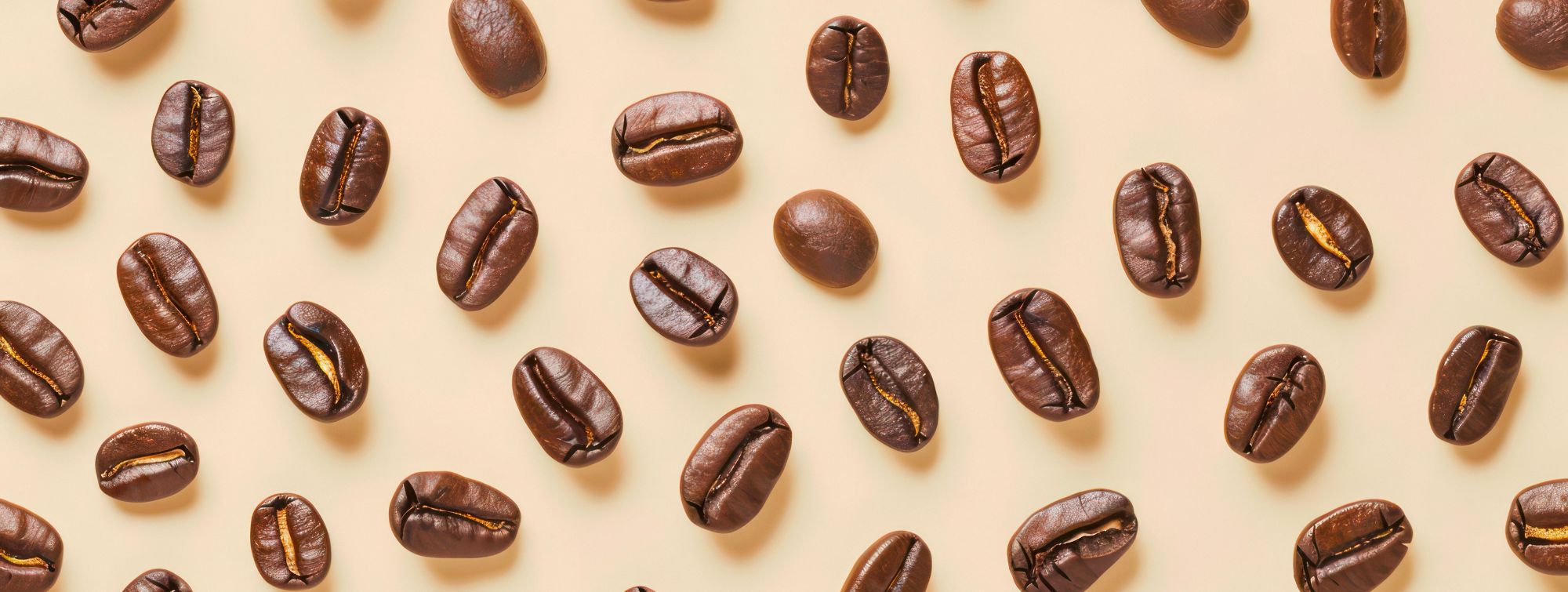 Coffee beans scattered on beige background, textured repeating pattern, warm and appetizing atmosphere.