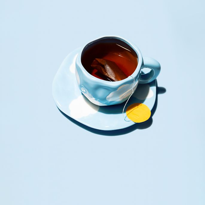 Cup of tea with teabag on blue saucer, top view on pastel blue background, minimalist and calming composition.
