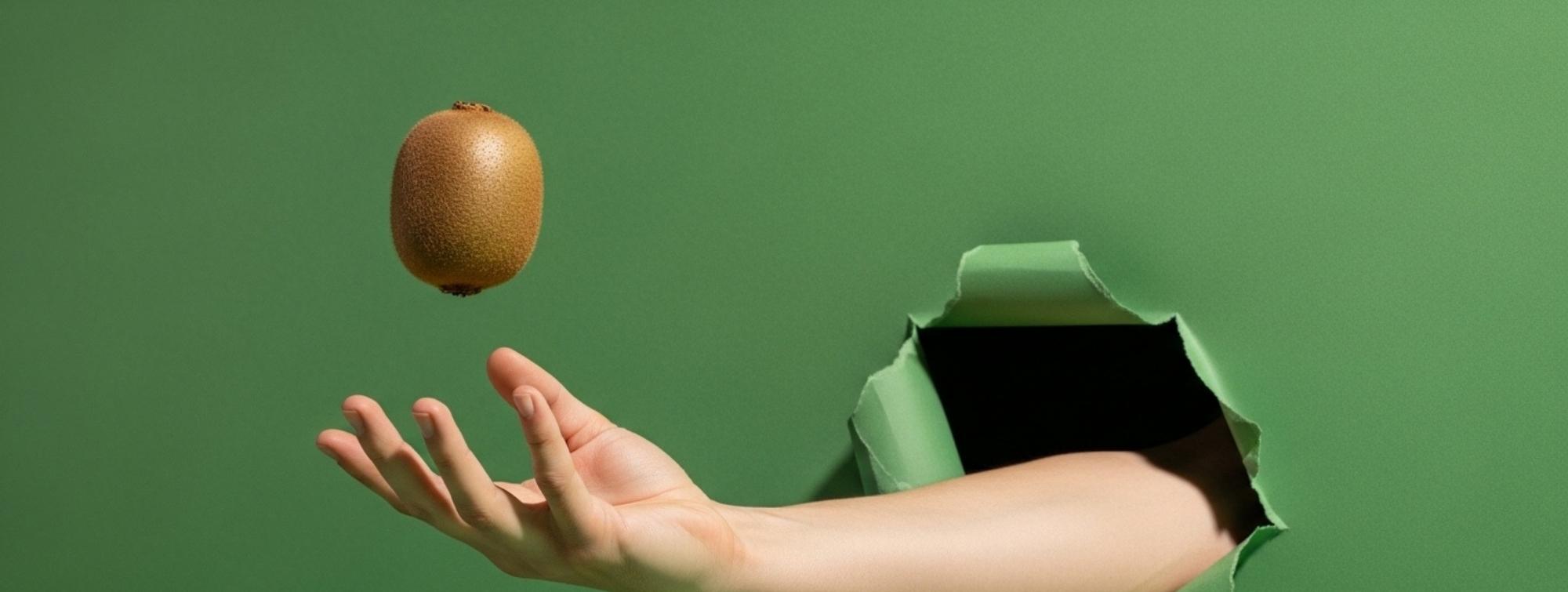 Hand emerging from torn green background tossing a kiwi in the air, minimalist composition with soft light and strong contrast