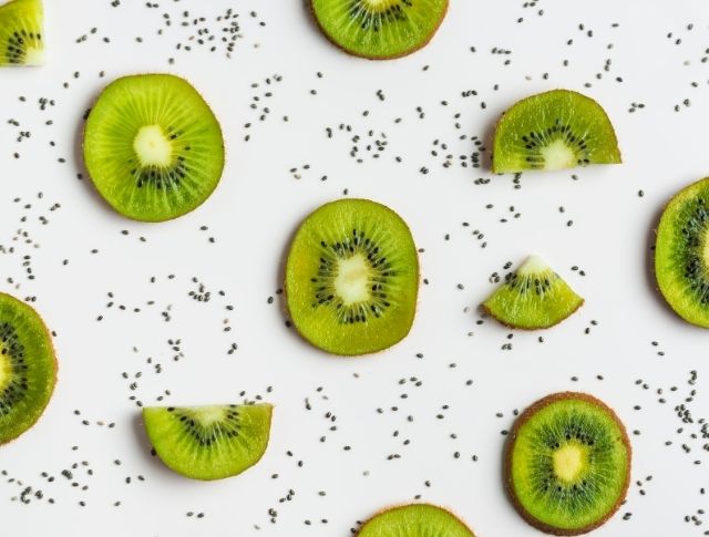 Kiwi slices arranged on white background with scattered chia seeds, minimalist graphic composition with repeating patterns