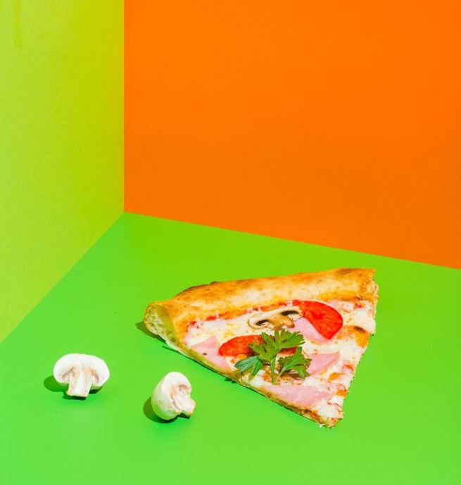 Slice of pizza with tomato, ham, and mushrooms on a green and orange background