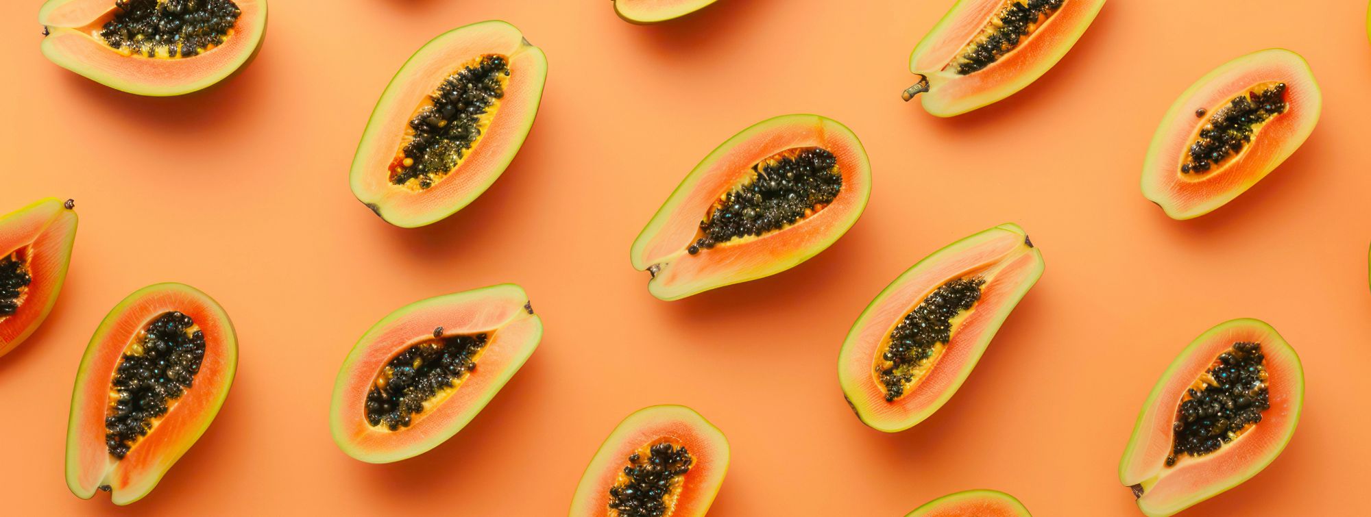 Papayas cut in half, showing their orange pulp with black seeds, on an orange background.