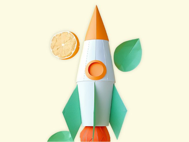Paper rocket in white, orange and green lying flat, surrounded by a half lemon slice and green paper leaves on a light yellowbackground.