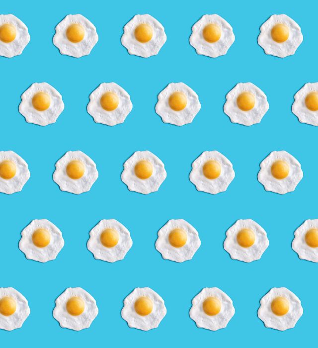 Pattern of fried eggs evenly arranged on blue background, minimalist and playful food design