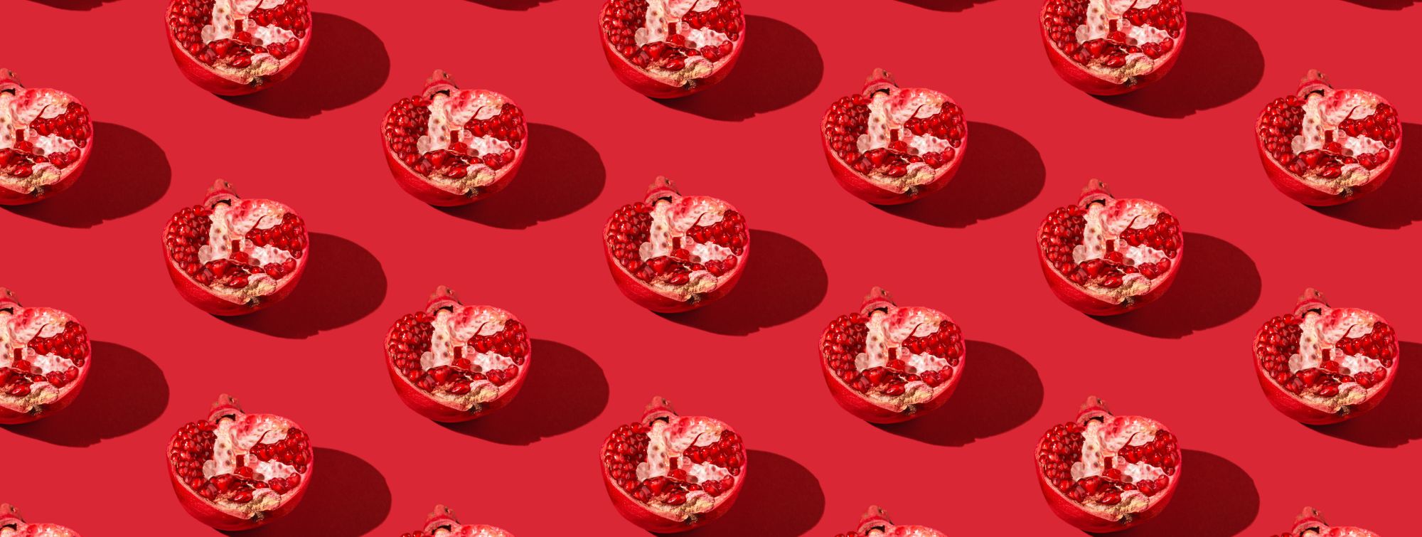 Pattern of open pomegranates showing red seeds on red background, vibrant and repetitive composition